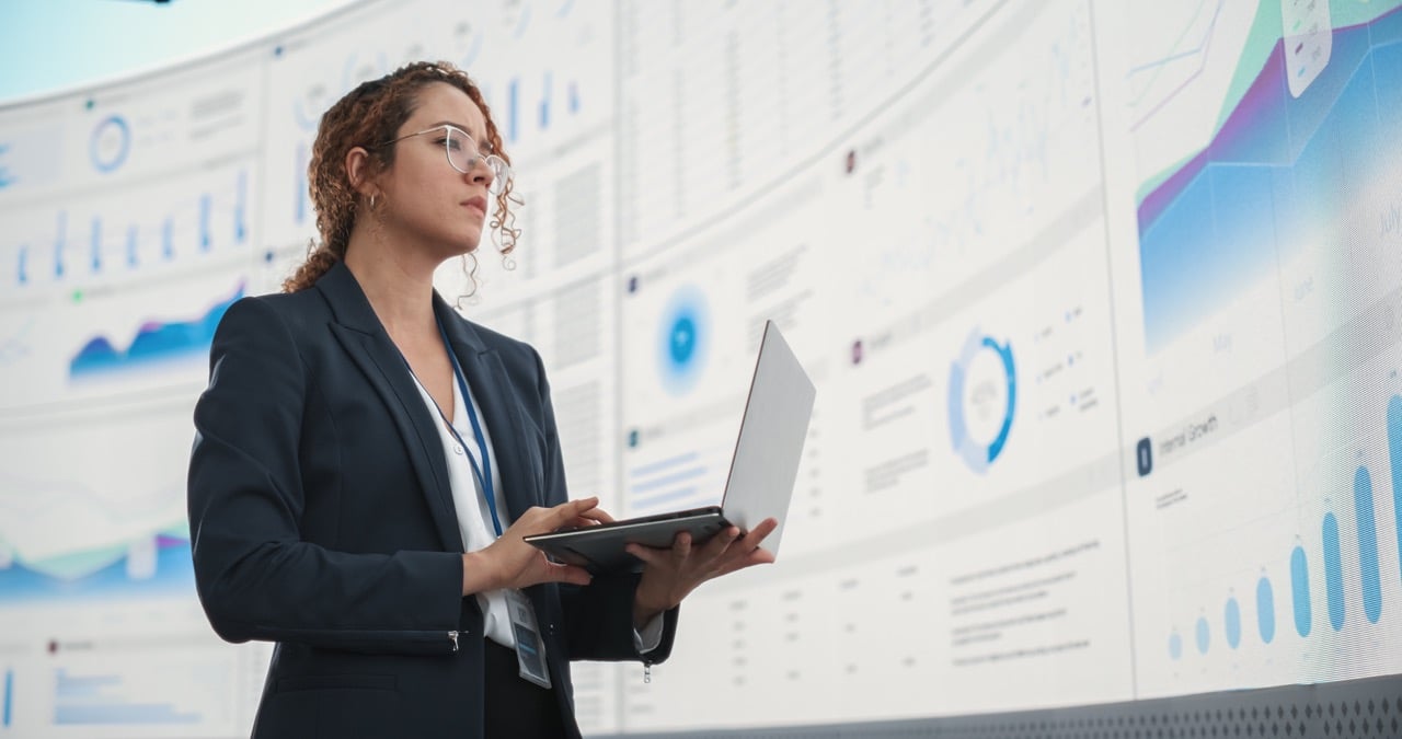 Successful Hispanic Businesswoman Holding Laptop Computer And Reviewing Debt Management Software Financial Reports On Digital Screen In Monitoring Office. 